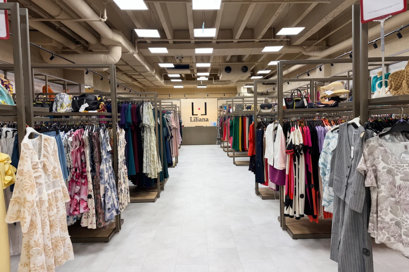 Sala de vânzare a magazinului Liliana Trade, cu culoarul central și peretele cu firma în fund